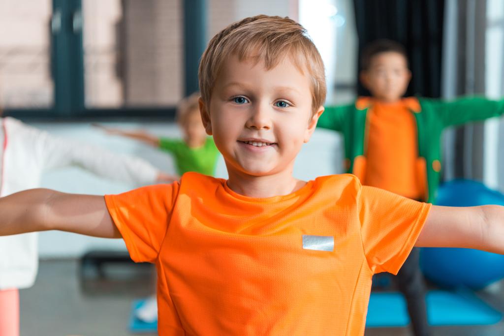 Enfoque selectivo del niño sonriendo y haciendo ejercicio con las manos extendidas en el gimnasio
 - Foto, Imagen