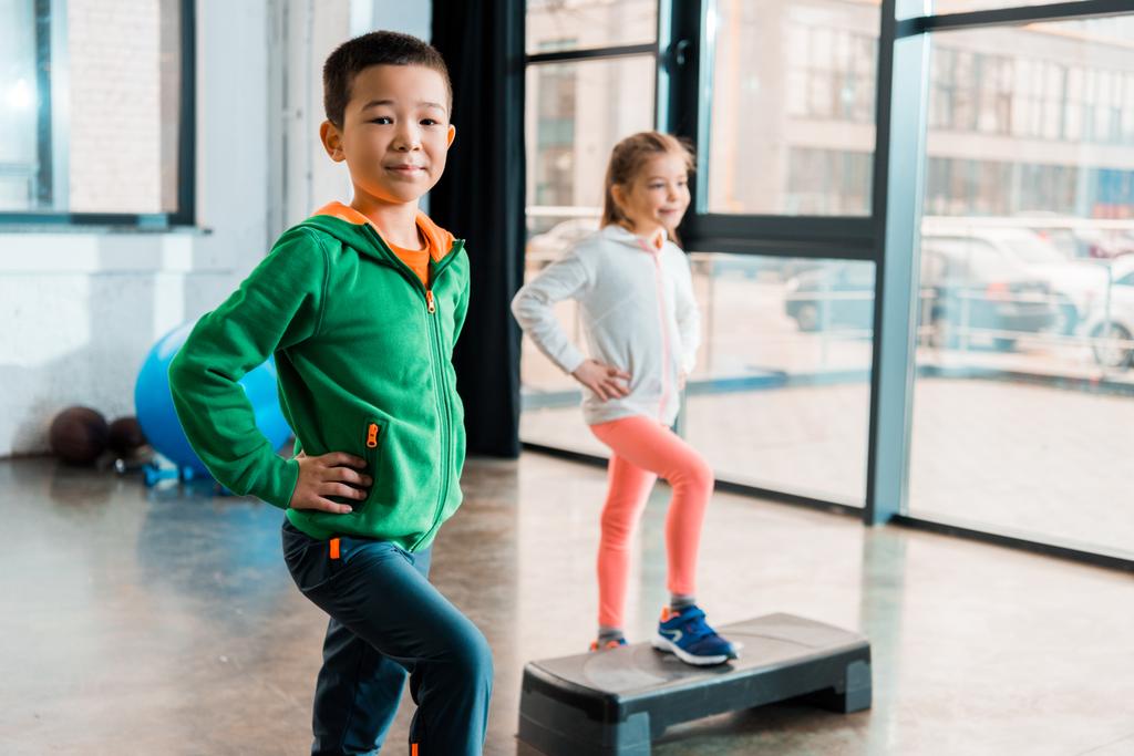 Вибірковий фокус мультикультурних дітей з руками на стегнах вправи на крокових платформах в тренажерному залі
 - Фото, зображення