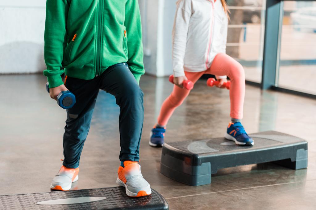 Vista recortada de niños sosteniendo pesas y ejercitándose en plataformas escalonadas
 - Foto, Imagen