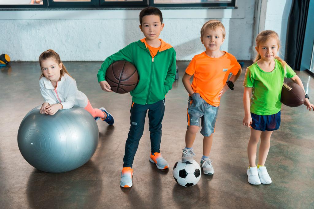 Дитина лежить на фітнес-кулі поруч з багатонаціональними дітьми з м'ячами в спортзалі
 - Фото, зображення