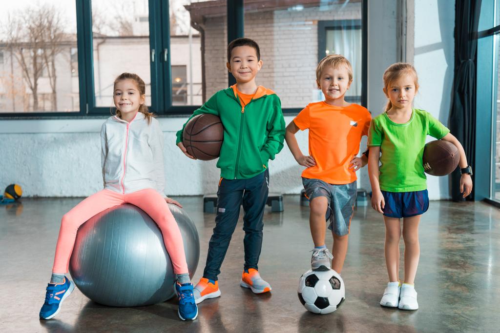 Vista frontal de Niño sentado en pelota de fitness junto a niños multiétnicos con pelotas en el gimnasio
 - Foto, imagen