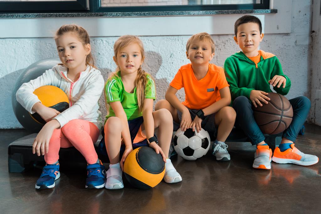 Multiculturele kinderen zitten op stapplatforms met ballen in de sportschool - Foto, afbeelding