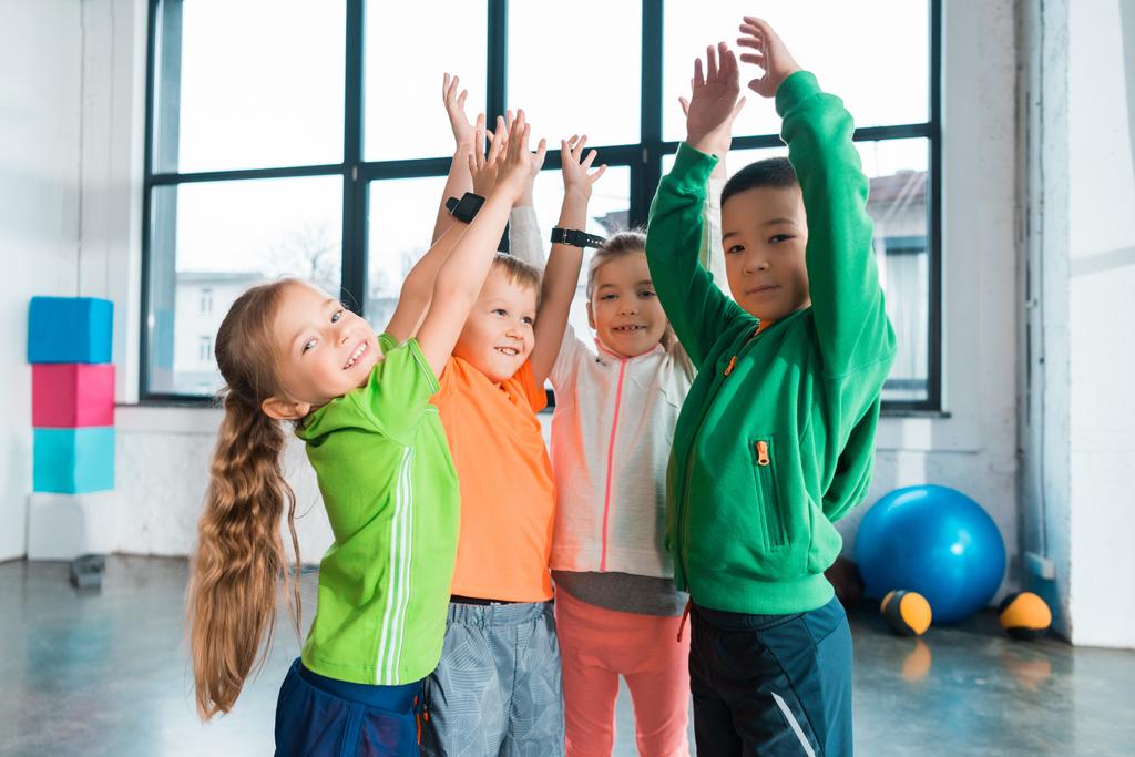 Πολυεθνικά παιδιά σηκώνουν τα χέρια ψηλά στο γυμναστήριο - Φωτογραφία, εικόνα
