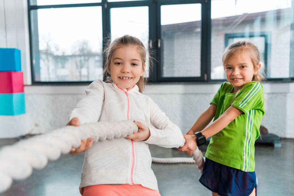 Селективное внимание детей, улыбающихся и играющих в перетягивание каната в спорткомплексе
 - Фото, изображение