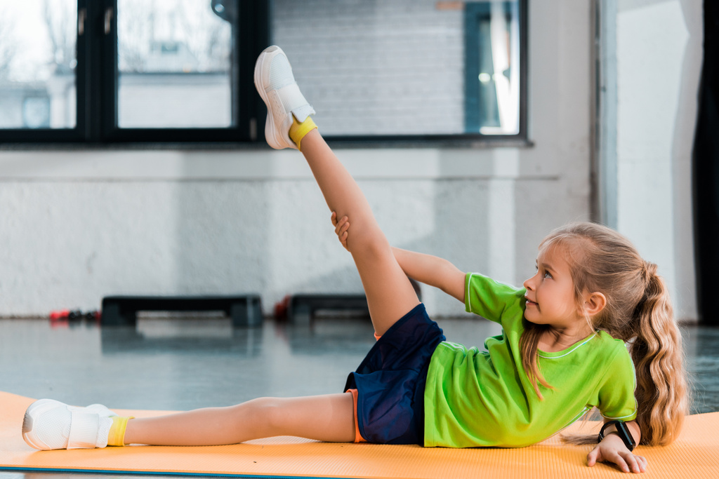 Selektiver Fokus des Kinderbeins beim Stretching auf der Fitnessmatte im Sportzentrum - Foto, Bild