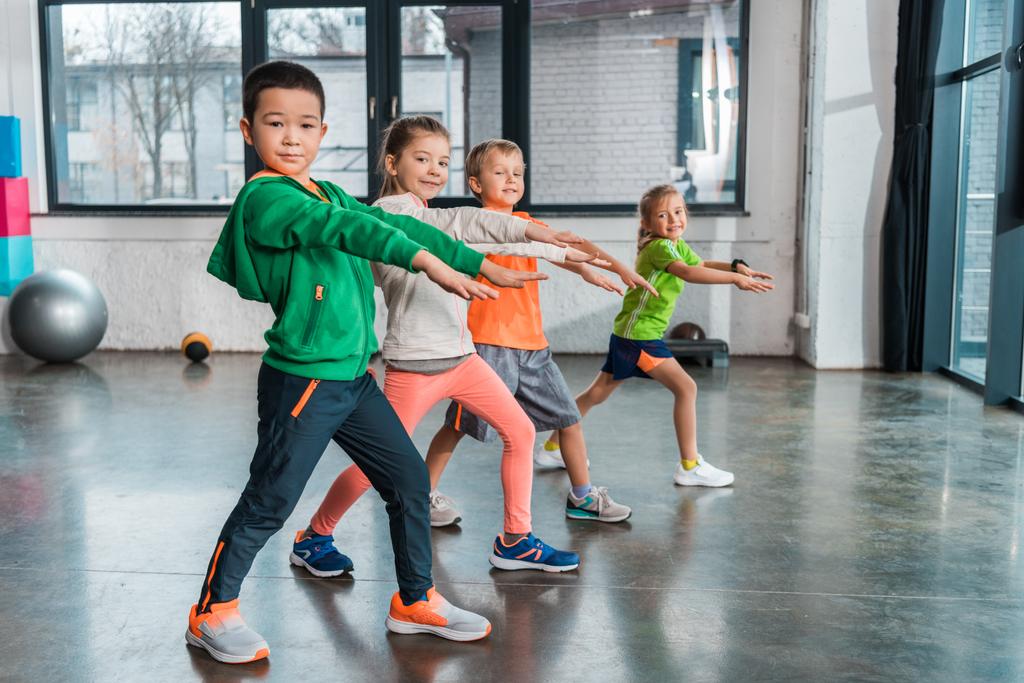 Side view of multiethnic children with outstretched hands doing lunges in gym - Photo, Image