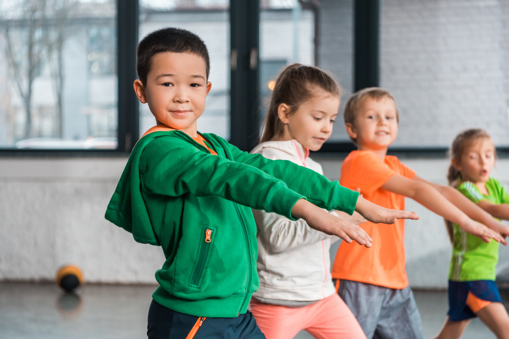 Selektiver Fokus multikultureller Kinder mit ausgestreckten Händen beim Turnen im Fitnessstudio - Foto, Bild