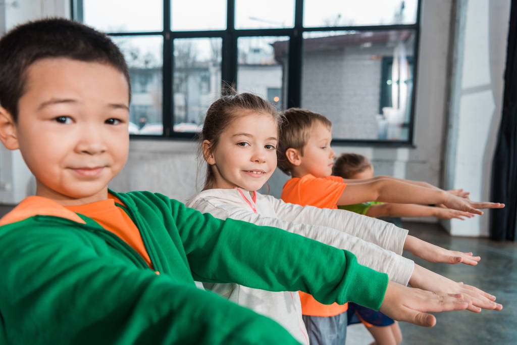 Багатокультурні діти з простягнутими руками дивиться на камеру в спортзалі
 - Фото, зображення