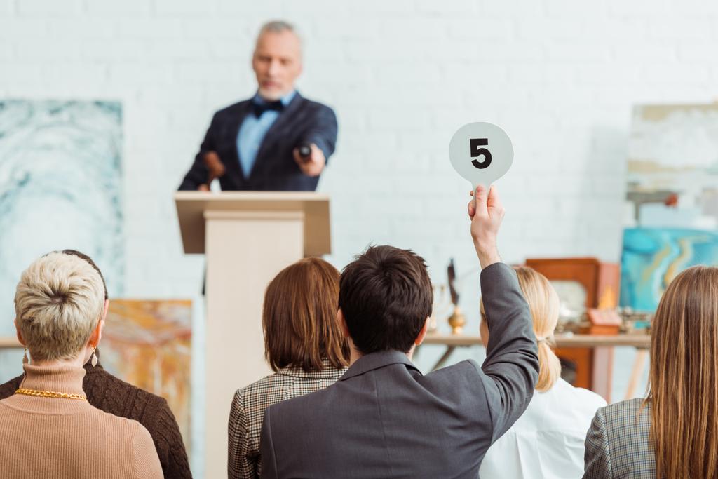 back view of buyer showing auction paddle with number five to auctioneer during auction - Photo, Image