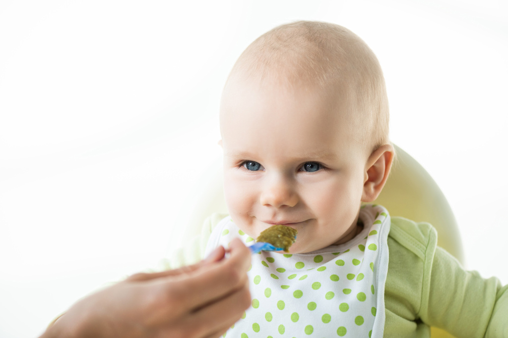 Selective focus of infant looking at mother with spoon while eating on feeding chair isolated on white - Photo, Image