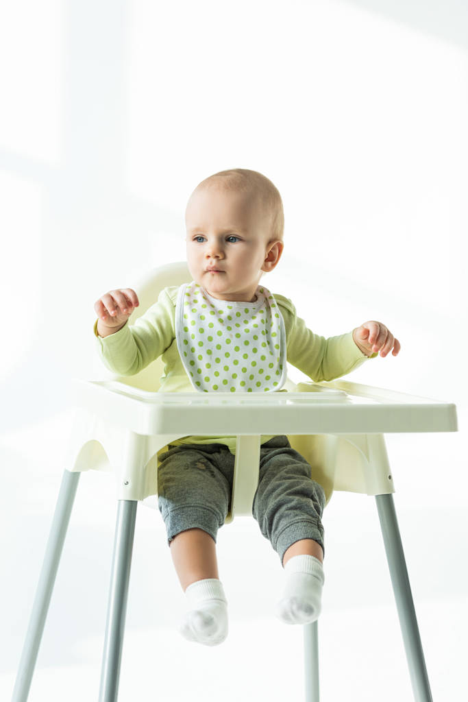 Vauva istuu ruokintatuolilla ja katsoo pois valkoisella taustalla
 - Valokuva, kuva