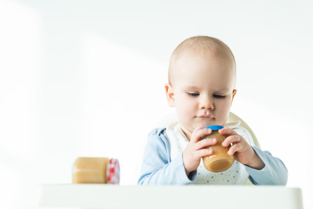 Concentration sélective de bébé mignon avec des pots de nourriture pour bébé sur la table de la chaise d'alimentation sur fond blanc
 - Photo, image