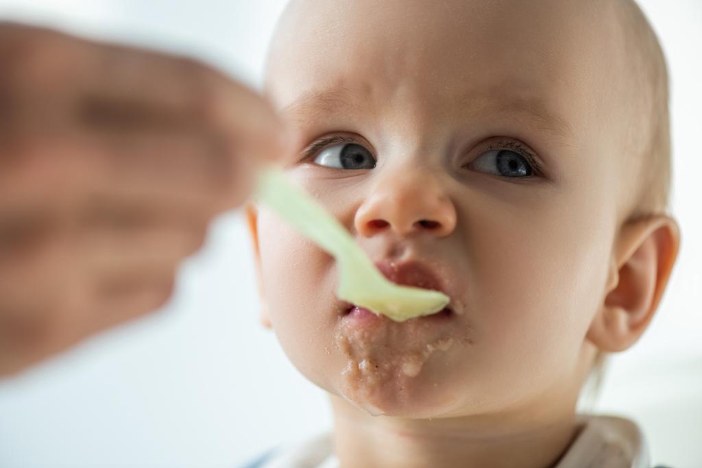 Selectieve focus van moeder voeden baby met puree op grijze achtergrond - Foto, afbeelding