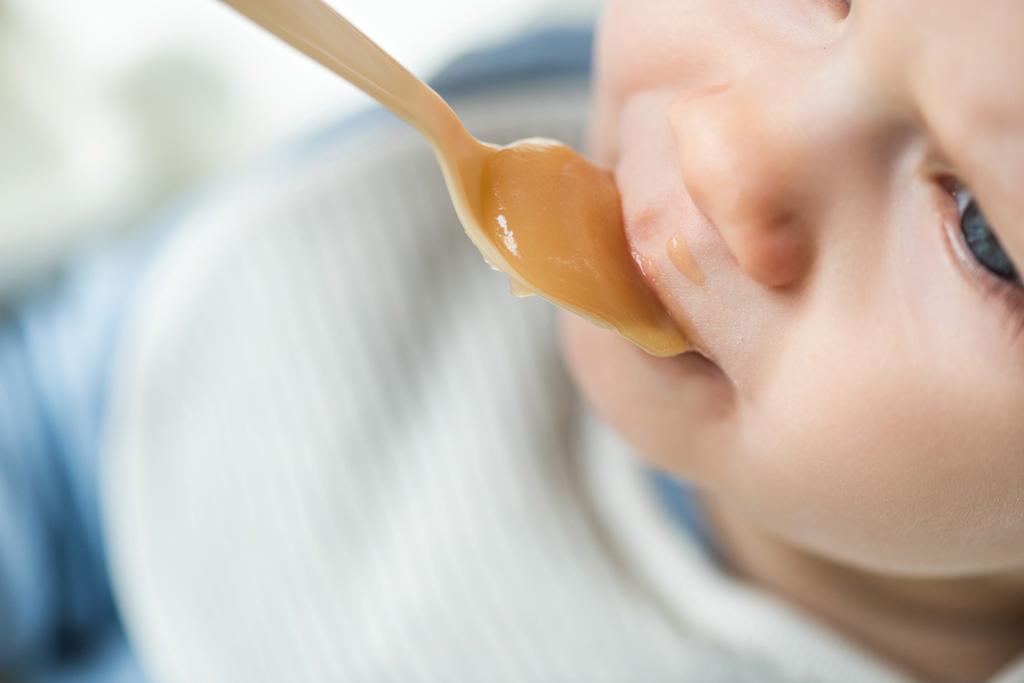Hochwinkel-Ansicht des Jungen während der Fütterung von Früchten Babynahrung auf weißem Hintergrund - Foto, Bild