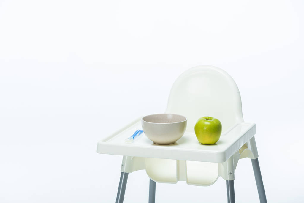 Schüssel mit Löffel und reifem Apfel auf Tisch des Futterstuhls isoliert auf weiß - Foto, Bild