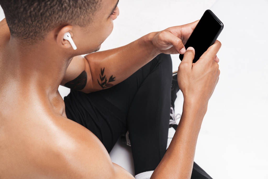 Zdjęcie Afrykańskiego Amerykanina używającego telefonu komórkowego i nauszników podczas siedzenia - Zdjęcie, obraz