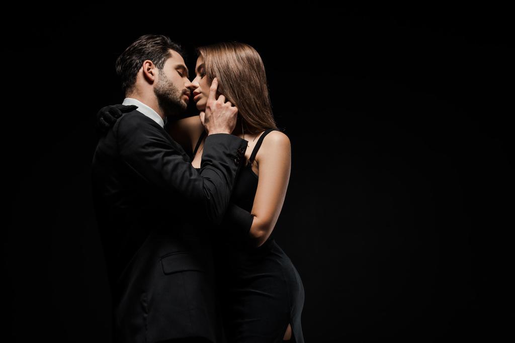 side view of handsome man touching face of attractive woman in dress isolated on black  - Photo, Image