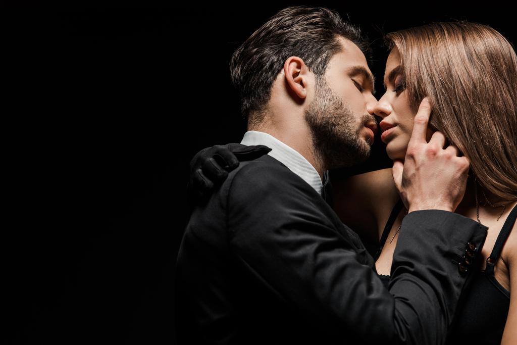 Seitenansicht eines hübschen Mannes im Anzug, der eine attraktive Frau auf Schwarz küsst  - Foto, Bild
