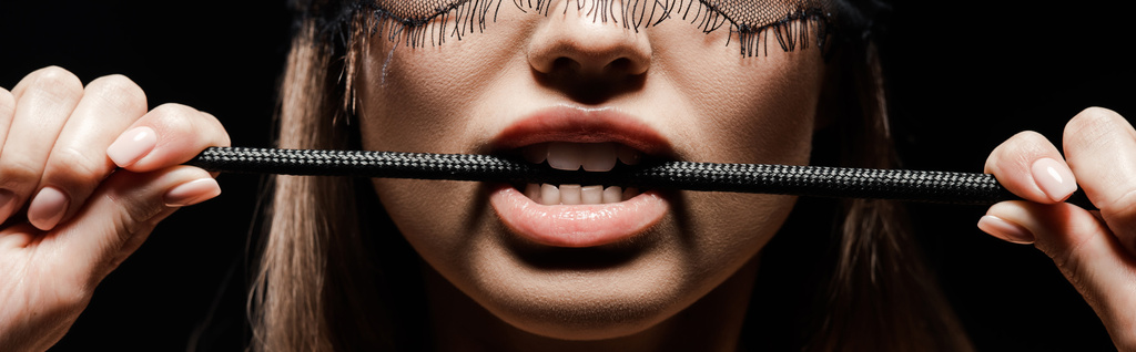 tiro panorâmico de mulher segurando chicote açoitamento na boca isolado no preto
  - Foto, Imagem