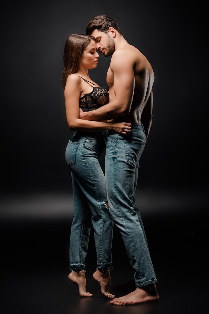 side view of sexy couple in blue jeans standing on black  - Photo, Image
