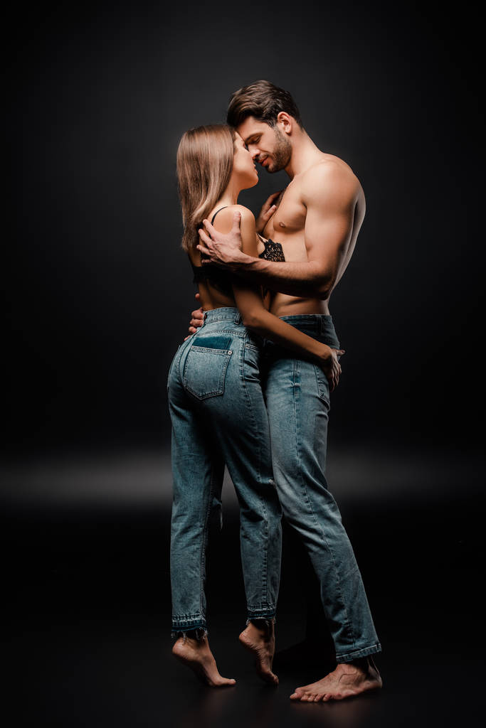 muscular man hugging seductive girl in jeans on black  - Photo, Image