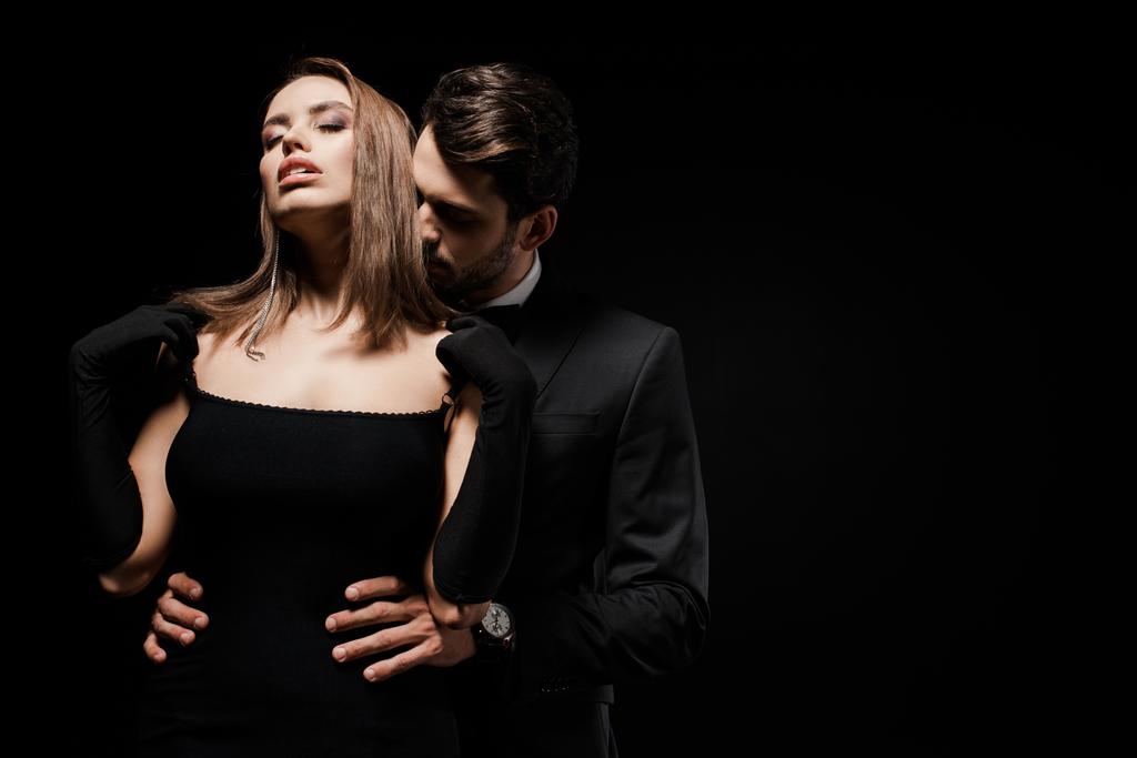 homem bonito em terno abraçando mulher atraente com olhos fechados isolado em preto
  - Foto, Imagem