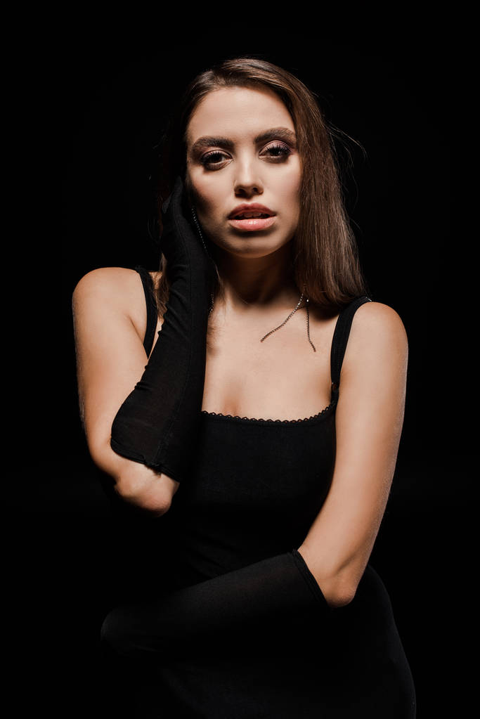 ελκυστική γυναίκα με γάντια κοιτάζοντας κάμερα απομονωμένη σε μαύρο  - Φωτογραφία, εικόνα