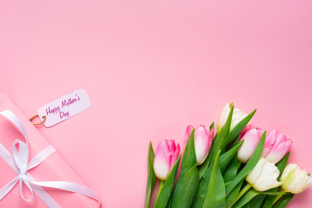 Widok z góry prezent z szczęśliwy dzień matki napisy na papierze etykieta w pobliżu tulipany na różowym tle - Zdjęcie, obraz