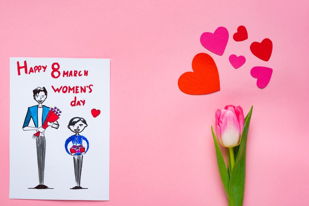 Κάτοψη της ευχετήριας κάρτας με σχέδιο και 8 Μαρτίου ευτυχισμένη γυναικεία ημέρα γράμματα και τουλίπα με χάρτινες καρδιές σε ροζ φόντο - Φωτογραφία, εικόνα