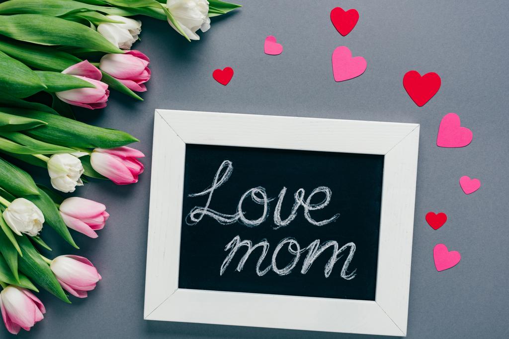 Kreidetafel von oben mit Liebe-Mama-Schriftzug, Papierherzen und Tulpen auf grauem Hintergrund - Foto, Bild