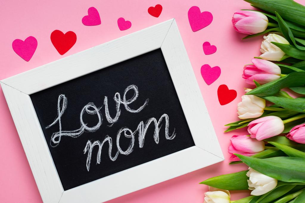 Top view of chalkboard with love mom lettering near paper hearts and tulips on pink background - Photo, Image
