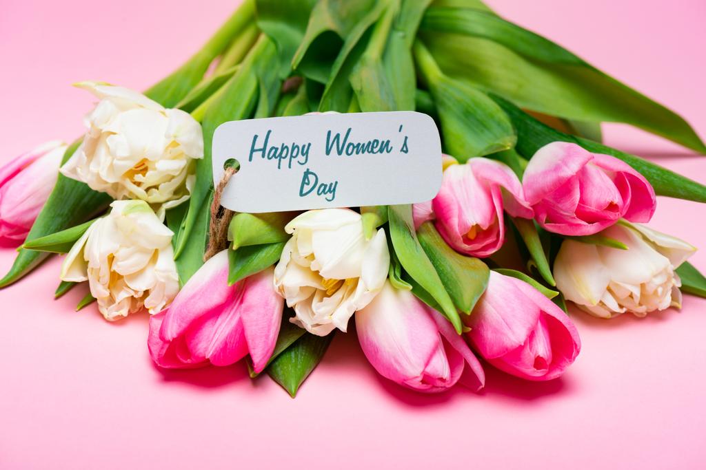 Beschriftung glücklicher Frauentag auf Papieretikett auf Tulpenstrauß auf rosa Hintergrund - Foto, Bild