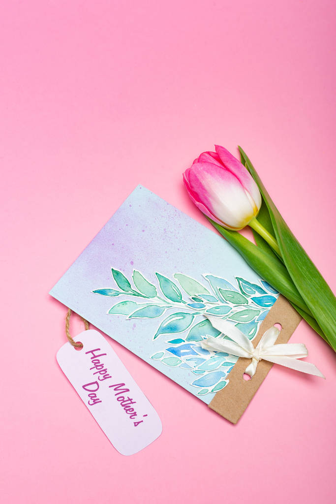 Draufsicht der Zeichnung Grußkarte mit glücklichem Muttertag Schriftzug auf Papieretikett und Tulpe auf rosa Hintergrund - Foto, Bild
