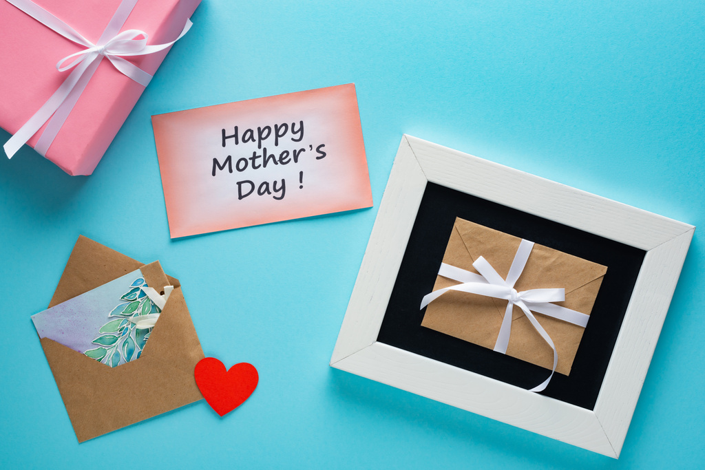 Vue du dessus de la boîte cadeau, enveloppes et cartes de vœux avec lettrage heureux de la fête des mères sur fond bleu
 - Photo, image