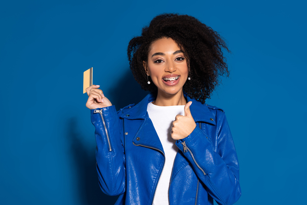 onnellinen afrikkalainen amerikkalainen nainen luottokortilla näytetään peukalo ylös sinisellä taustalla
 - Valokuva, kuva