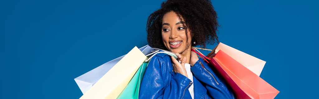 hymyilevä afrikkalainen amerikkalainen nainen ostoskassit eristetty sininen, panoraama laukaus
 - Valokuva, kuva