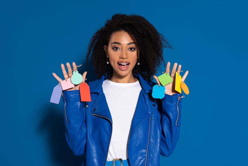 african american woman with open mouth and empty labels on hands on blue background - Photo, Image