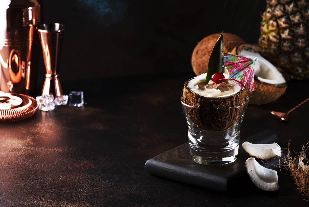 Cocktail Pina Colada em coco picado com frutas tropicais e ferramentas de bar, conceito de relaxamento de verão, espaço de cópia
 - Foto, Imagem