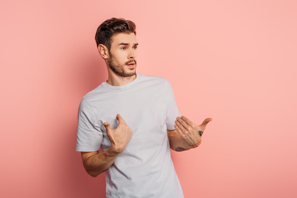 shocked young man looking away and pointing with hands at himself on pink background - Photo, Image