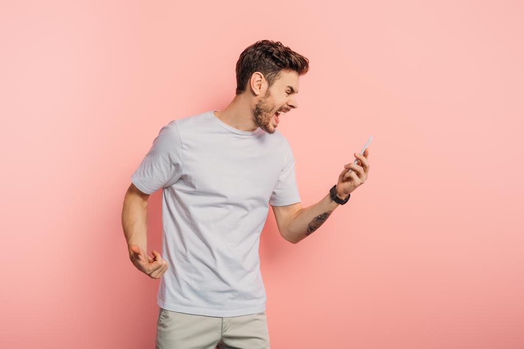 ärtynyt nuori mies huutaa samalla, kun videopuhelu älypuhelimella vaaleanpunaisella taustalla
 - Valokuva, kuva