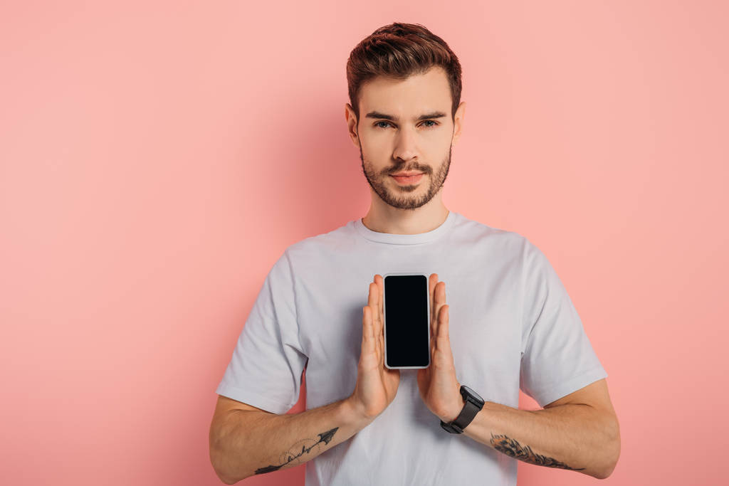 joven confiado mostrando teléfono inteligente con pantalla en blanco sobre fondo rosa
 - Foto, imagen