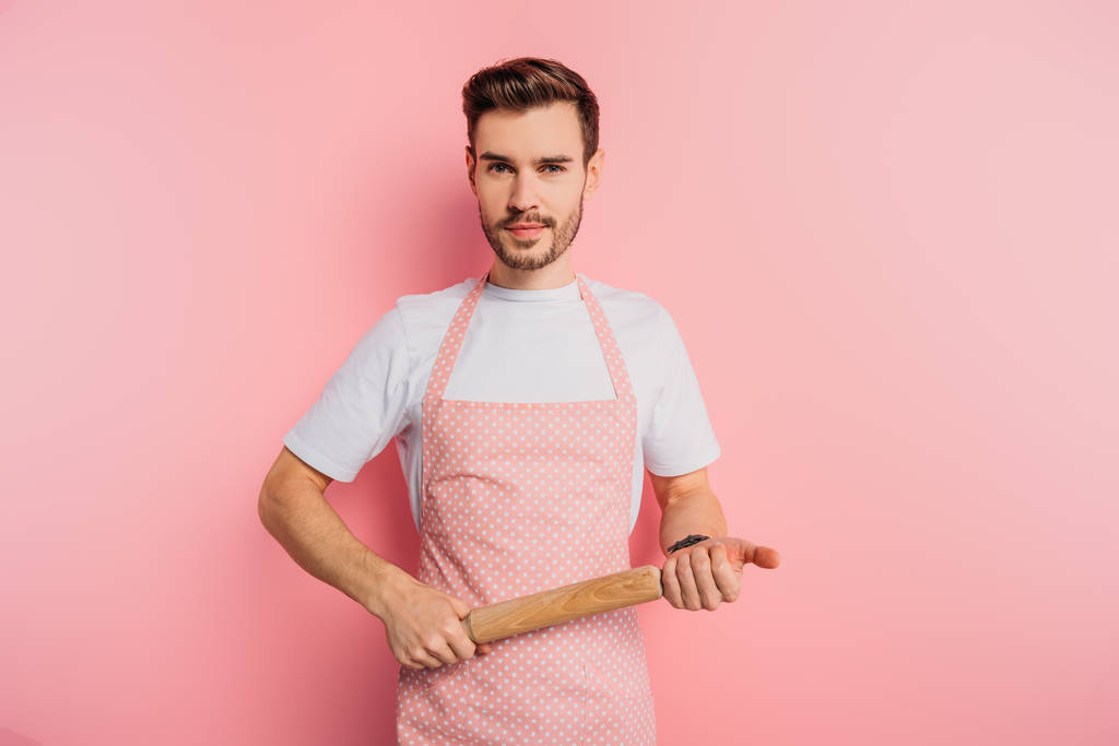 jovem confiante em avental segurando rolo de madeira no fundo rosa
 - Foto, Imagem