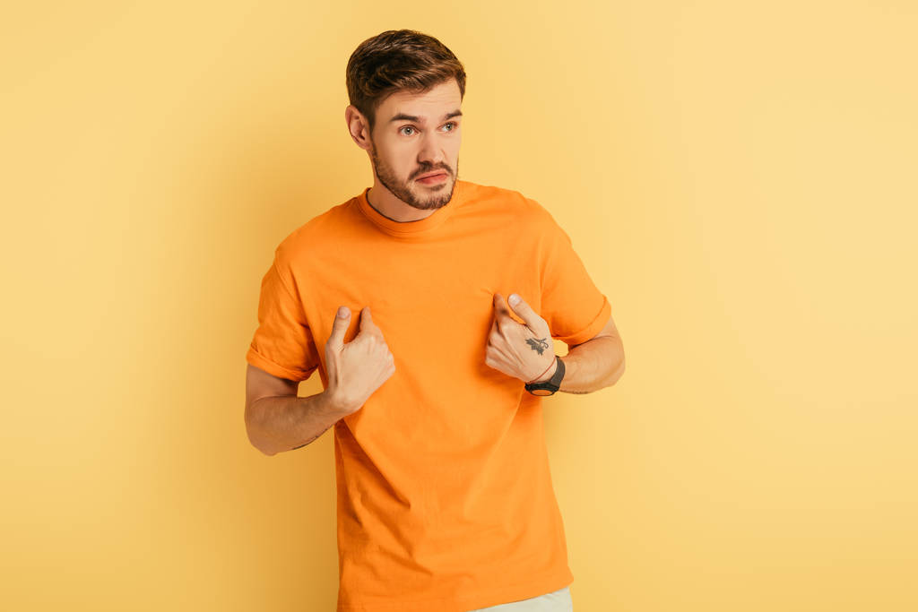 rozzlobený mladý muž ukazuje sám se sebou s prsty při pohledu pryč na žluté pozadí - Fotografie, Obrázek