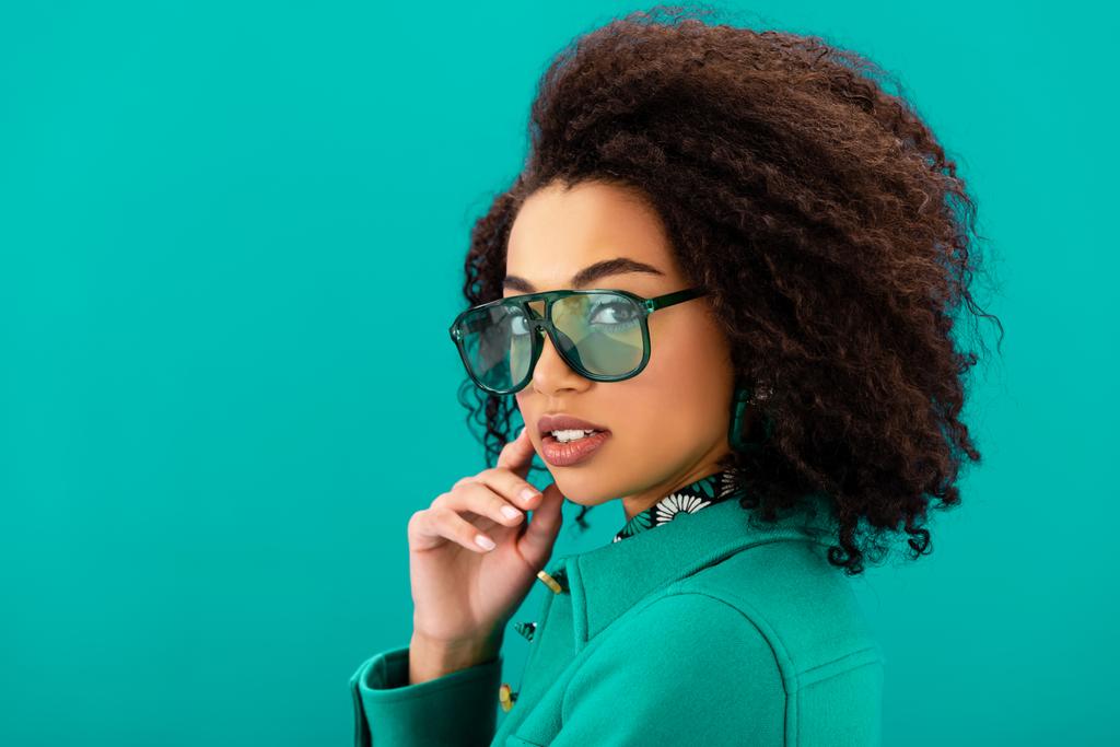 stylish african american woman in jacket looking at camera isolated on turquoise - Photo, Image