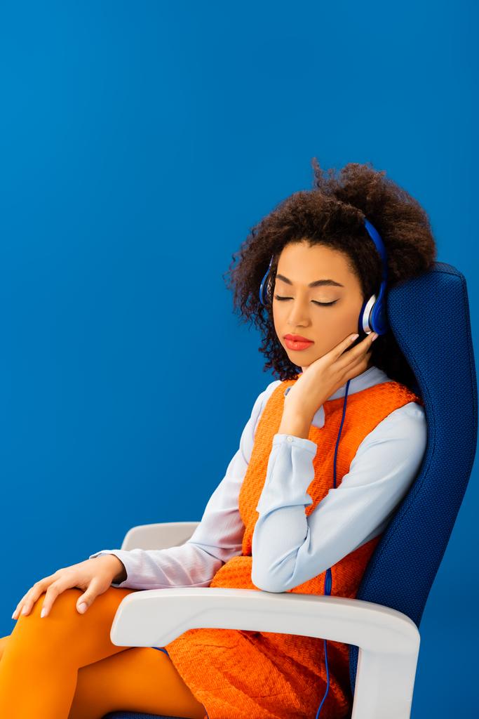 афроамериканський в ретро-сукні слухає музику і спить на сидінні ізольовано на синьому
  - Фото, зображення