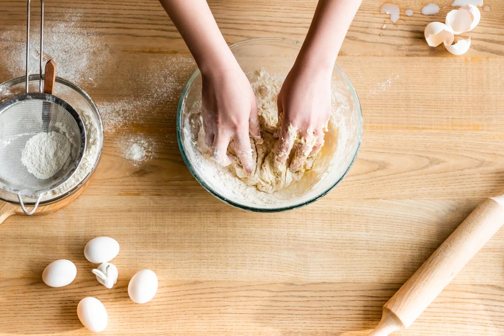 top view of woman kneading dough near flour in bowl, eggs and figurine with easter bunny   - Photo, Image
