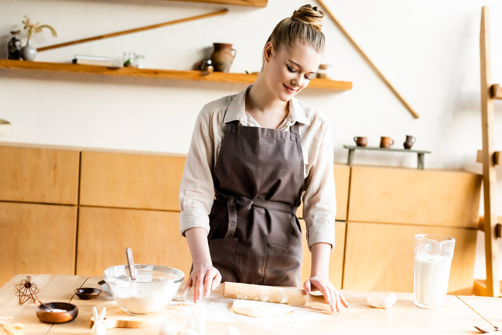Glückliche Frau rollt Teig mit Nudelholz in Küche aus  - Foto, Bild