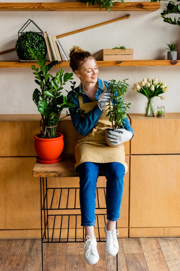 smiling young woman in apron holding green plant  - Fotoğraf, Görsel