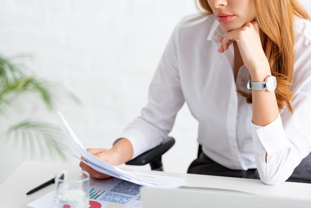 Vue agrandie d'une femme d'affaires tenant un dossier près de graphiques et d'un ordinateur portable sur une table - Photo, image