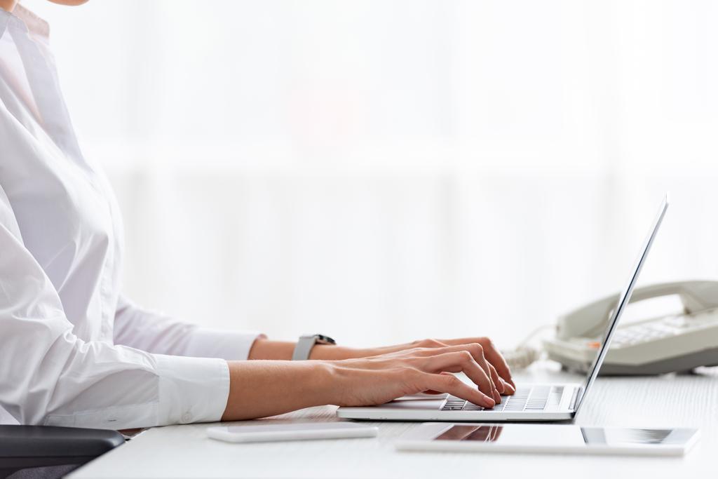 Vista recortada de la mujer de negocios utilizando el ordenador portátil cerca de gadgets en la mesa
 - Foto, Imagen
